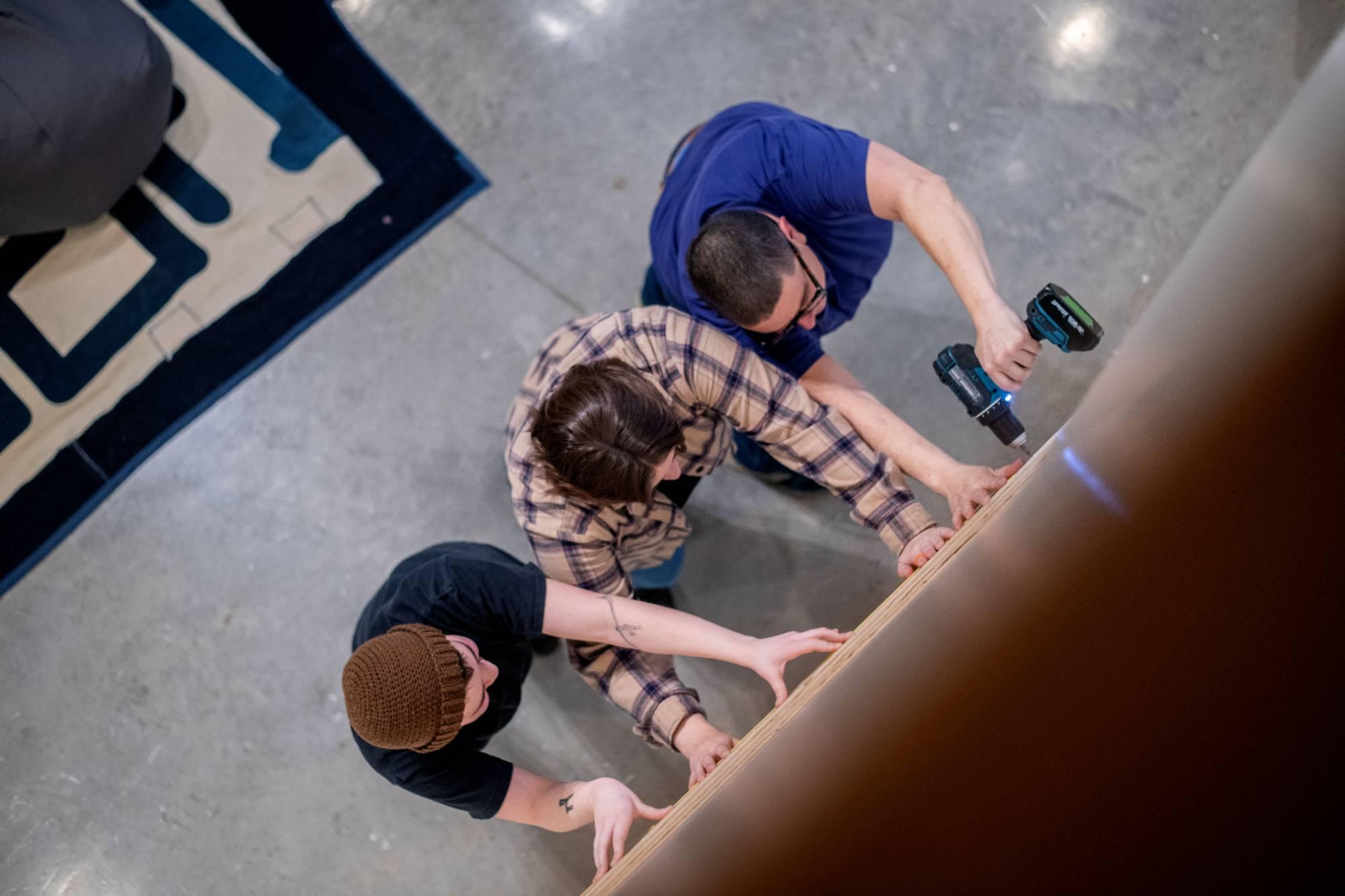 Students working to hang an image-based ceramic artwork with guest artist Emmy Bright.